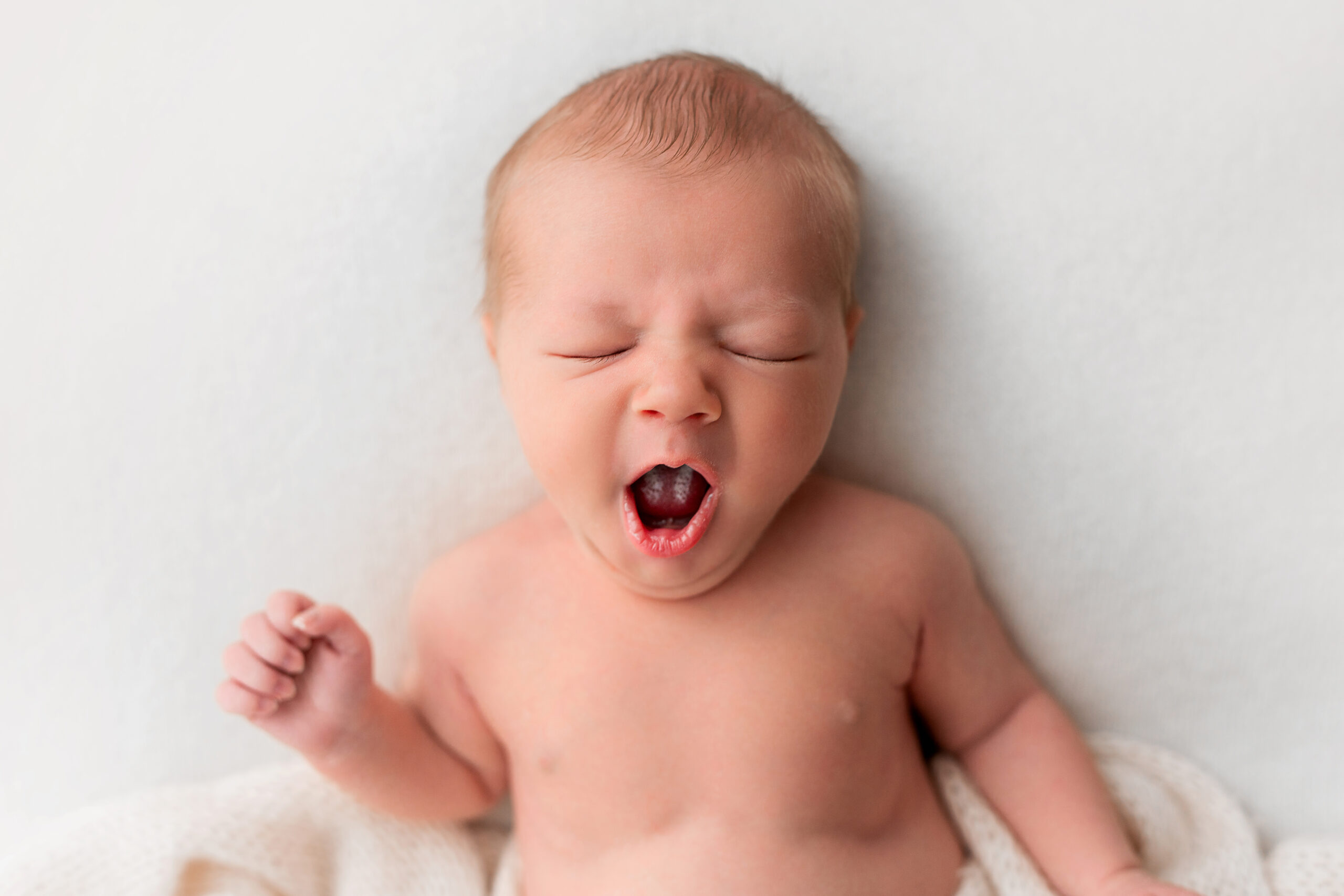 Baby Photographer Barnsley. A photo of a newborn baby laid yawning wide with his eyes tightly closed.